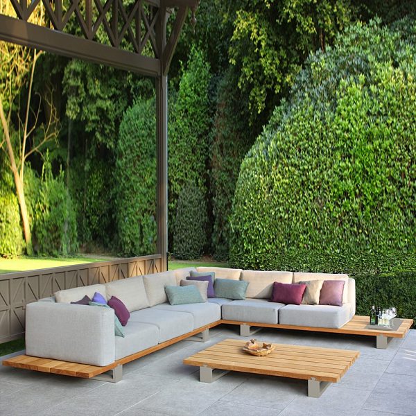 Image of Vigor teak corner sofa in pergola with extensive shrubs in background