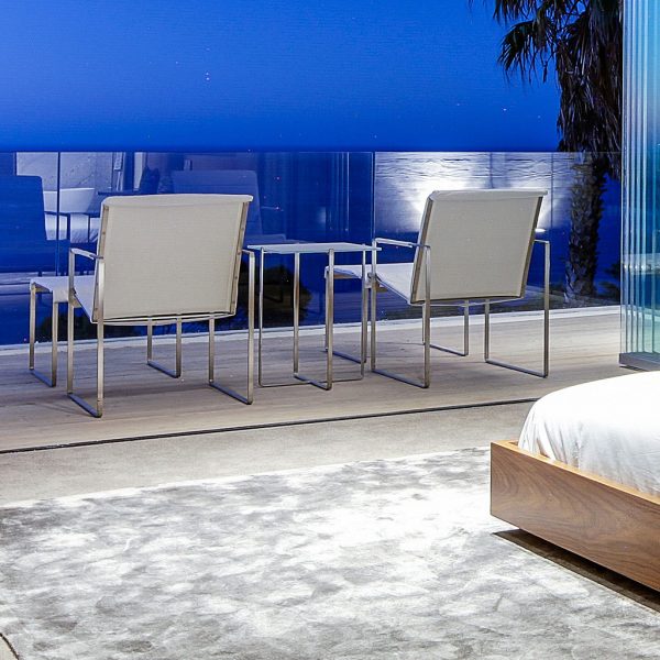 Nighttime image of pair of FueraDentro Poltrona contemporary outdoor lounge chairs and foot rests with EP stainless steel frames and white Batyline fabric surfaces