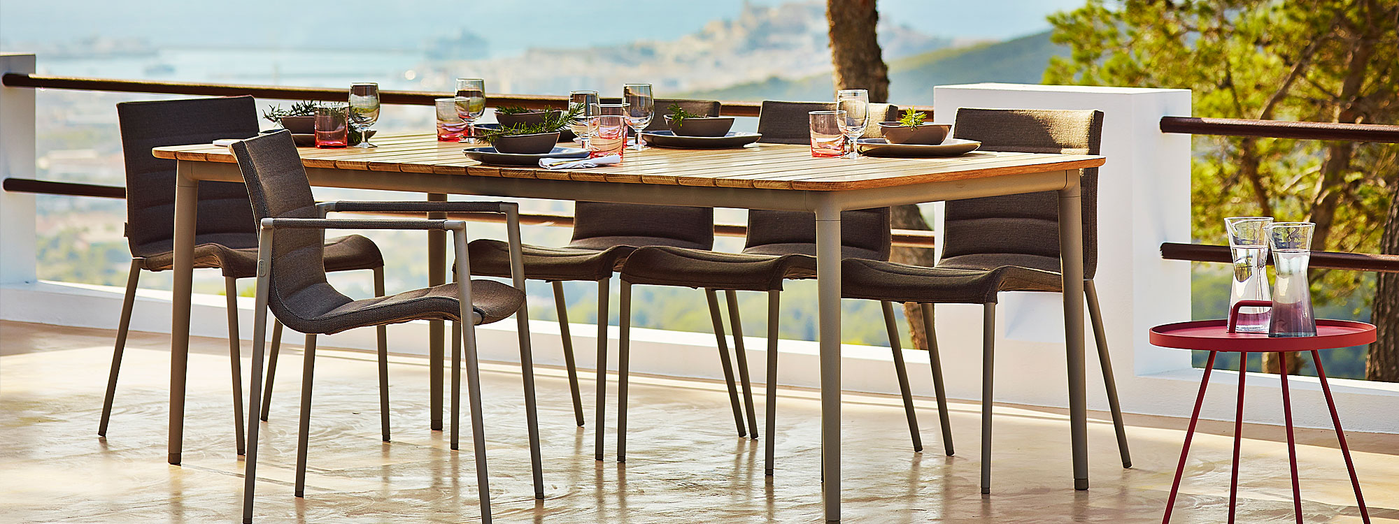 Image of taupe aluminum and teak Core dining table set for dinner, surrounded by Core upholstered dining chairs by Cane-line