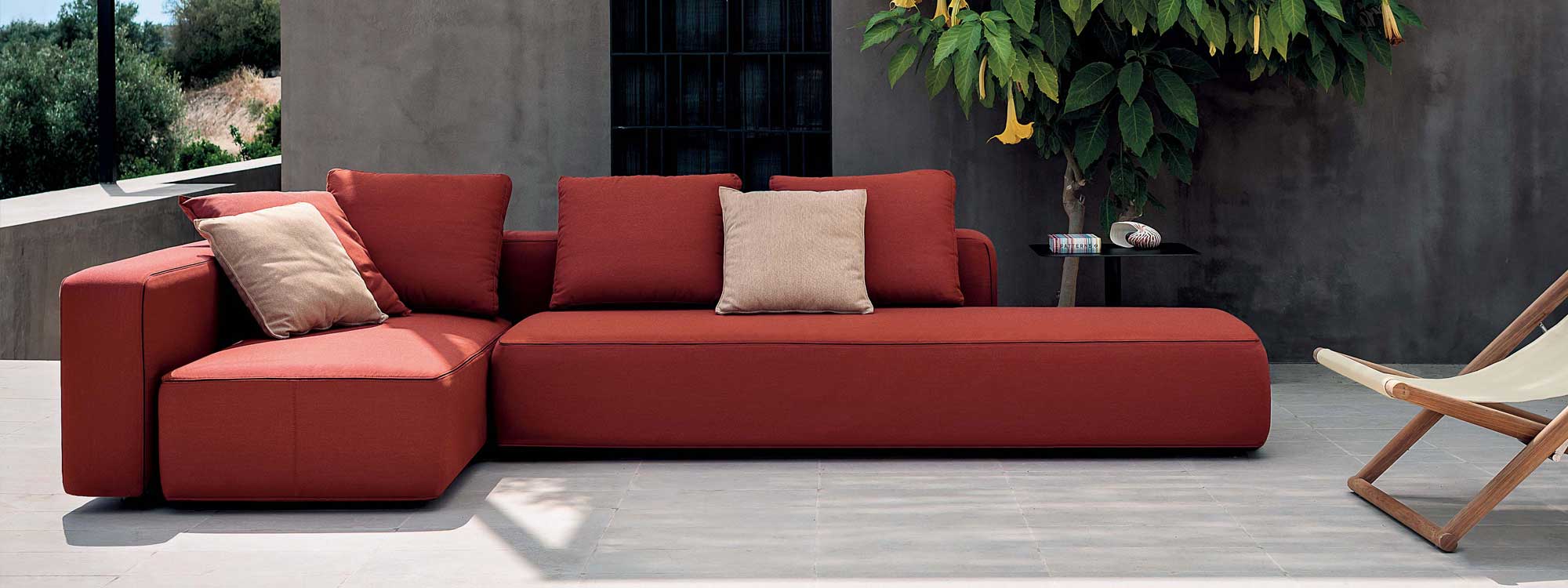 Image of Dandy red upholstered garden sofa on minimalist terrace with tree and poured concrete building in background