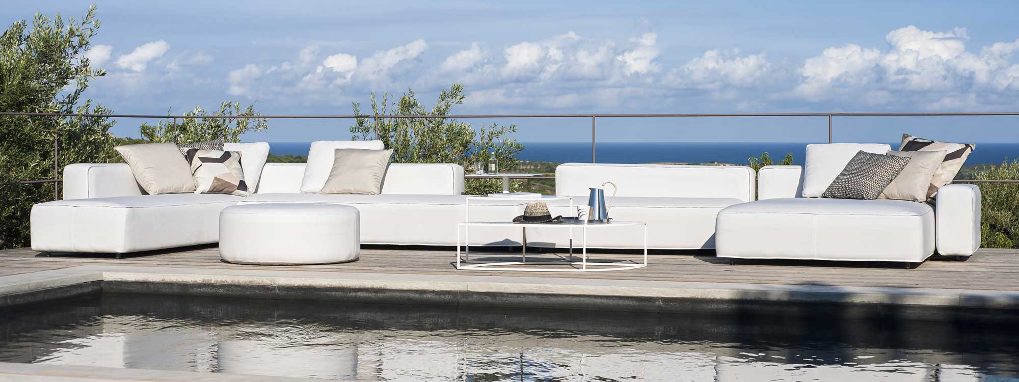 Large installation of white Dandy garden sofa next to swimming pool with sea in the background