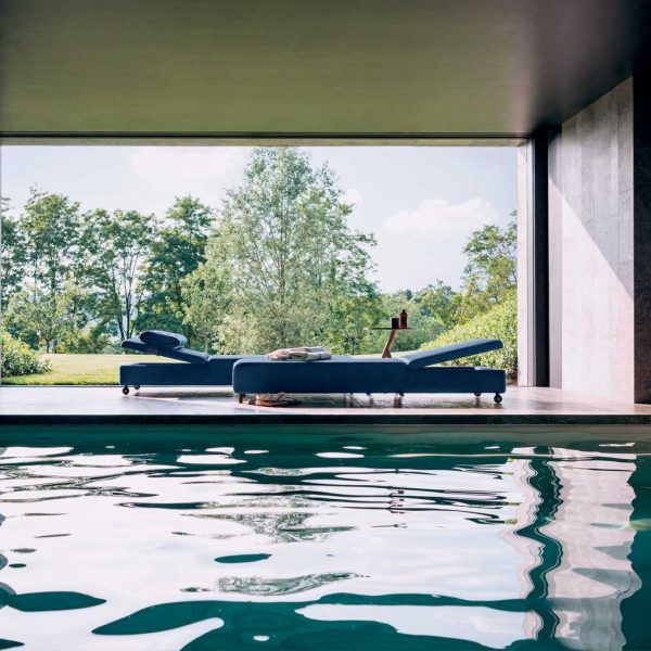 Image of Double blue sun loungers on indoor poolside with trees and lawn in the background