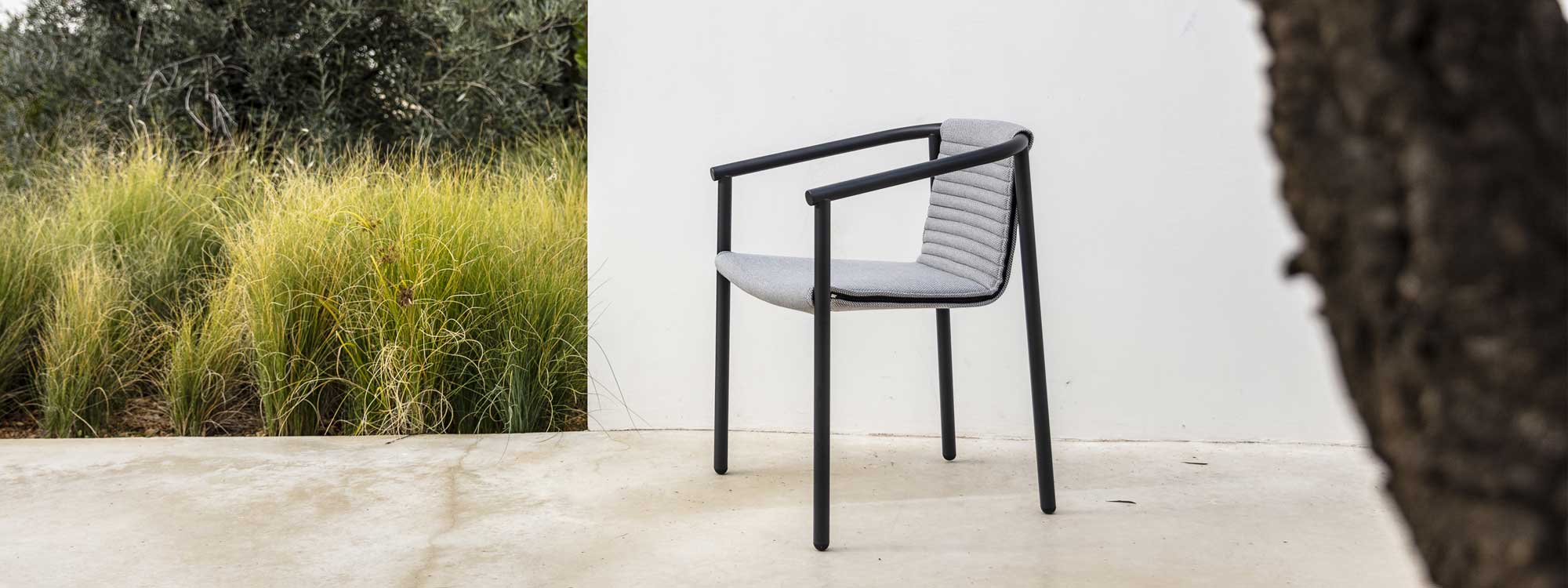 Image of anthracite colored Duct Round outdoor dining chair on poured concrete terrace next to grasses