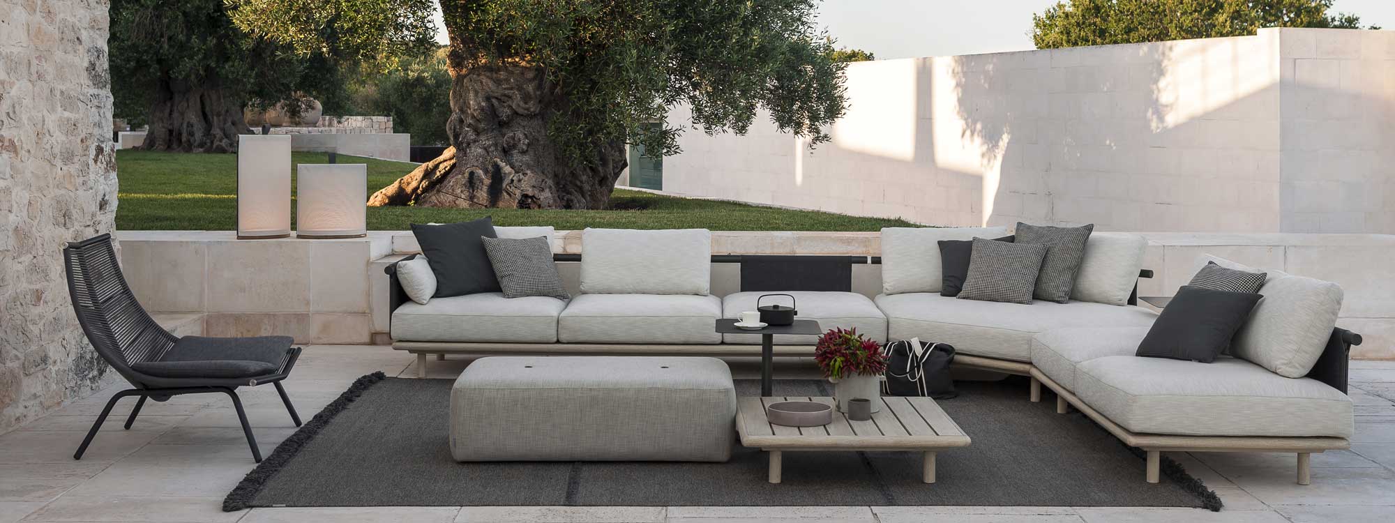Image of RODA Eden garden corner sofa with hexagonal corner unit, on white-washed terrace with lawn and ancient olive tree in the background