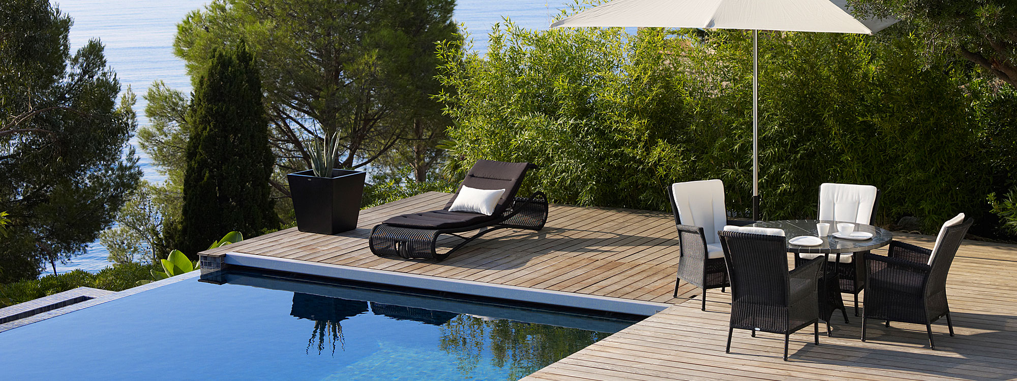 Escape Sun Lounger In Black Cane-line Weave next to swimming pool