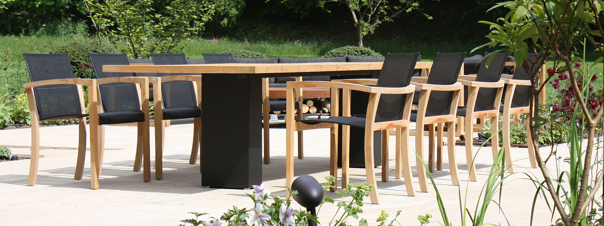 Image of Doble architectural garden table with black pedestal legs and teak top, together with XQI teak and Batyline garden chairs