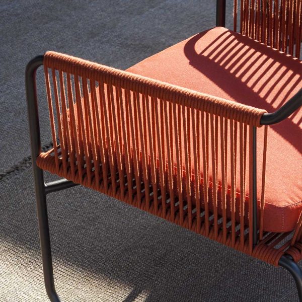 Image of detail of RODA Harp garden armchair with smoke colored frame and orange acrylic cord arm, with orange fabric cushion
