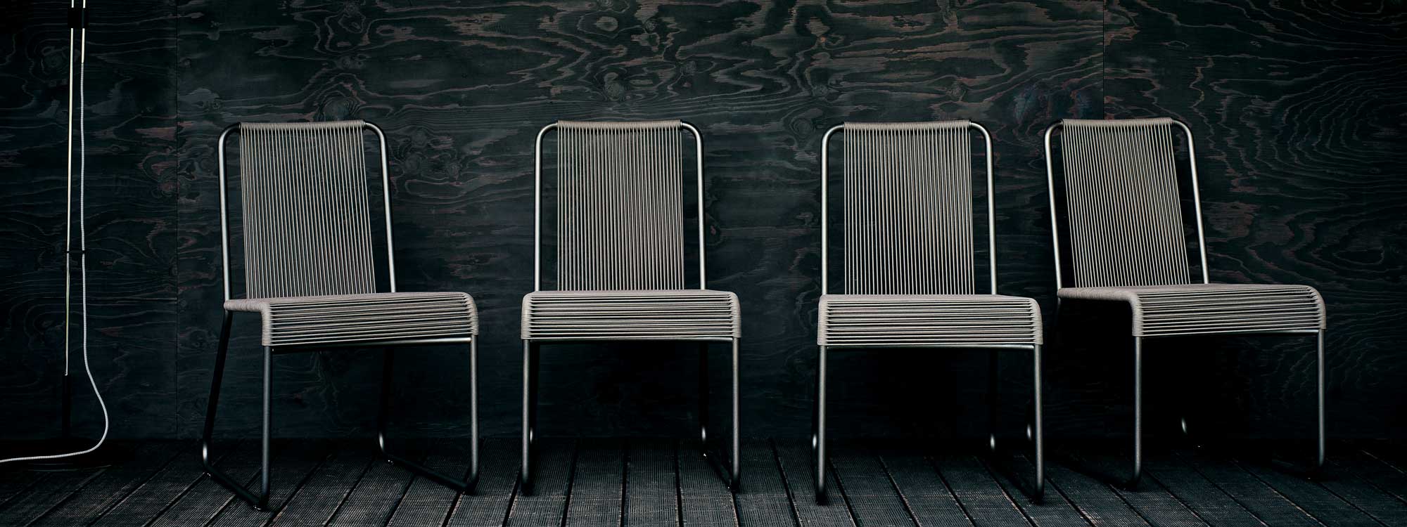 Image of 4 Harp black garden chairs with sand-colored rope seat and back by RODA, shown against black wooden wall