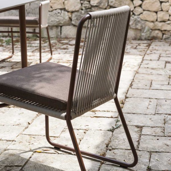 Image of Harp modern garden chair with rust colored tubular frame and sand colored rope seat and back, next to Piper extendable dining table by RODA