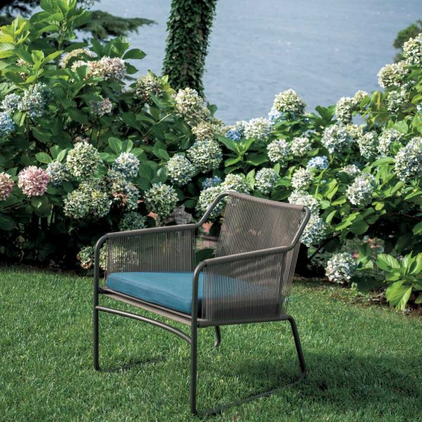 Image of RODA Harp modern garden lounge chair with tubular frame and back, seat and arms in acrylic cord, on lawn with Hydrangeas in background