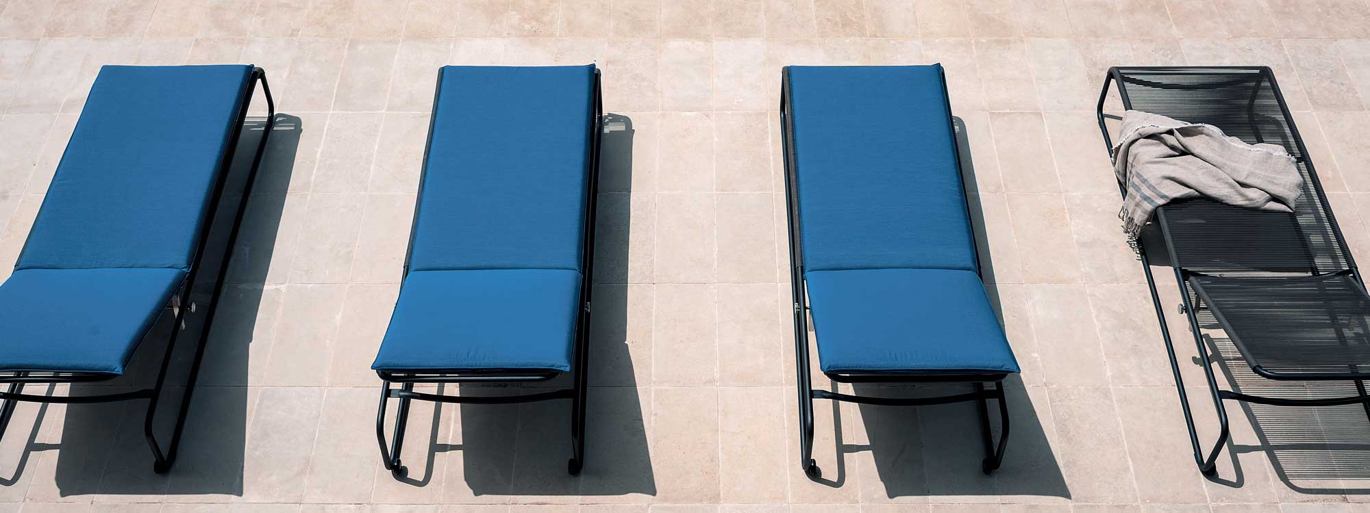 Image of row of Harp modern sun loungers with black tubular frames and blue cushions by RODA, on sunny terrace