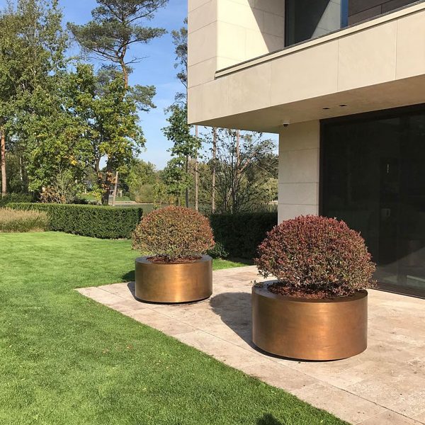 Image of pair of polished brass circular planters on terrace outside modernist house