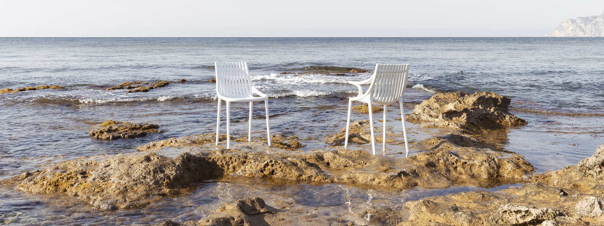 Image of pair of Vondom Ibiza chairs in white recycled plastic, shown on rocky Spanish coastline