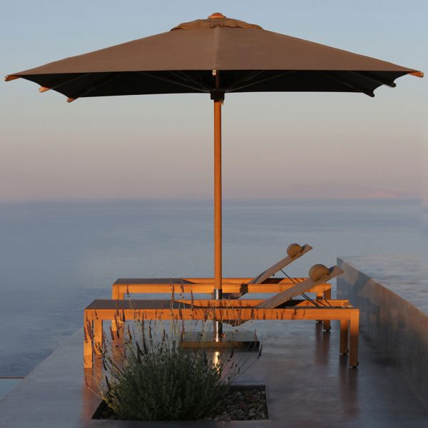 Image of pair of XQI sun loungers and Shady teak parasol by Royal Botania, on terrace at dusk, high above the ocean below.