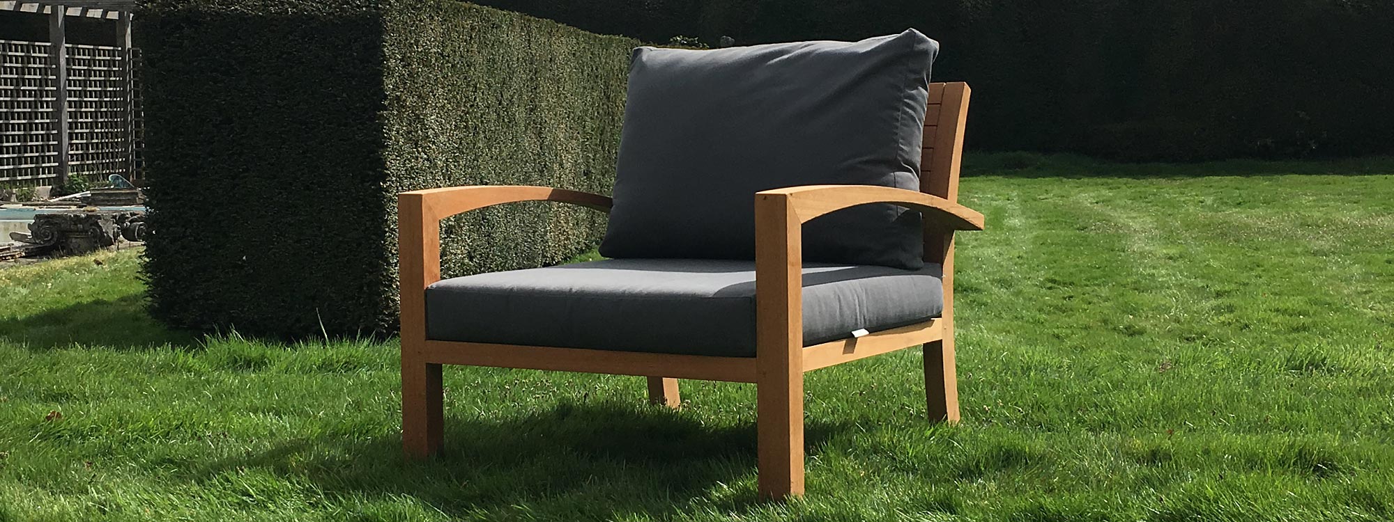 Image of IXIT teak relax armchair with grey back & seat cushions on verdant green lawn with yew hedge in background