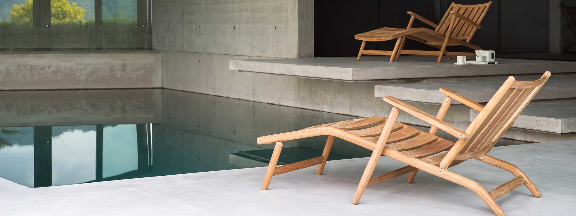 Image of pair of RODA Levante modern teak steamer chairs on minimalist poured concrete poolside