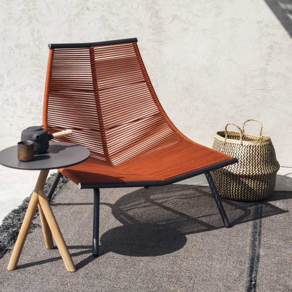 Image of RODA Laze modern outdoor lounge chair with smoke colored frame and orange cord seat and back, next to Stork teak side table
