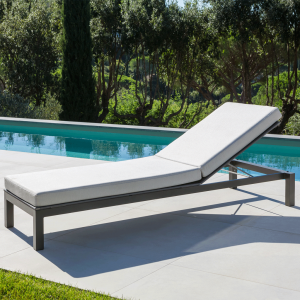 Image of Leuven dark-grey sun lounger with white cushion, with shrubs and still waters of swimming pool in the background