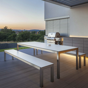 Dusk picture of Leuven garden table and benches in brushed stainless steel with White HPL surfaces on decked terrace