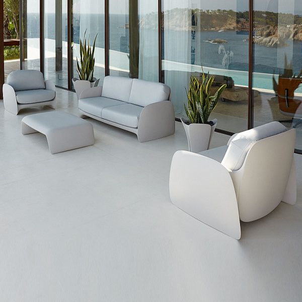 Image of Pezzettina organic garden sofa and lounge chairs by Vondom on balcony, with the sea reflecting in the glass behind the furniture