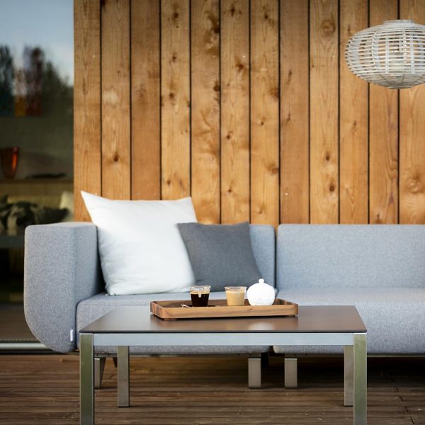 Image of Lotos outdoor sofa on wooden veranda, showing the furniture's shaped arm cushion