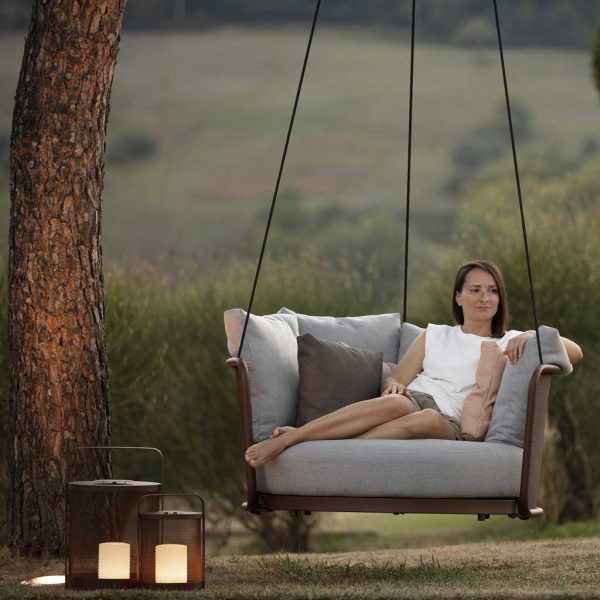 Image of woman sat in Todus Baza swing seat beneath tree at dusk, with Luci lanterns on floor to her side