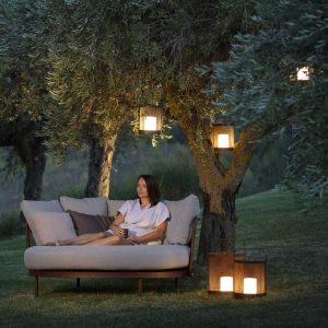 Woman sat on Baza modern garden daybed with Luci LED garden lanterns above and beside her