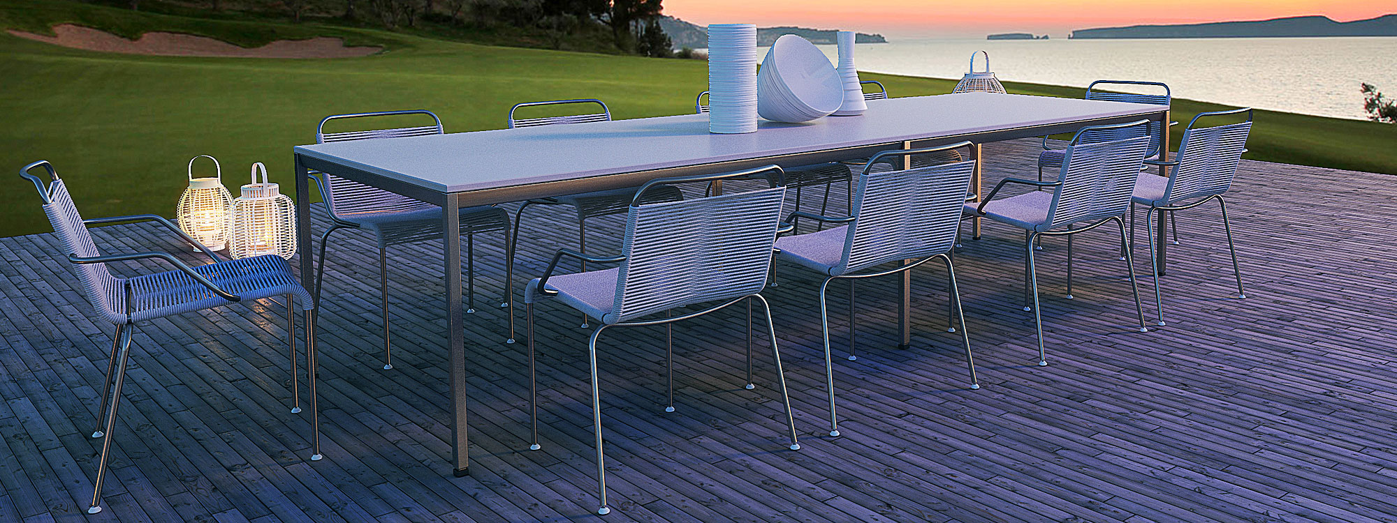 Image of Coro Jubeae stainless steel garden armchairs around long rectangular dining table on decking at sunset