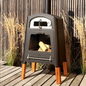 Image of M-Classic modern garden pizza oven in black lacquered stainless steel with iroko legs, shown on wooden decking with architectural grasses in the background