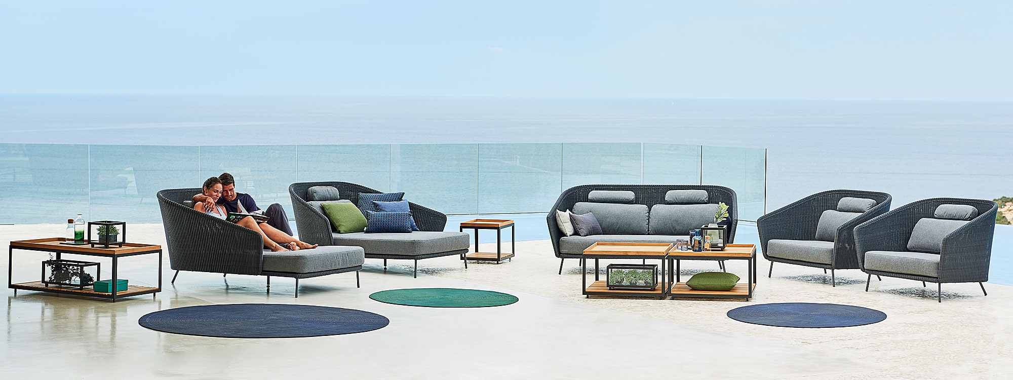 Image of couple relaxing in dark-grey Mega daybeds, next to Mega 2 seat garden sofa and lounge chairs by Cane-line