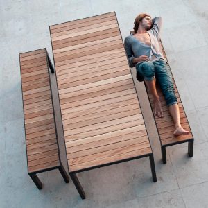 Dude in cardigan lying on Roshults modern garden bench in teak & anthracite stainless steel