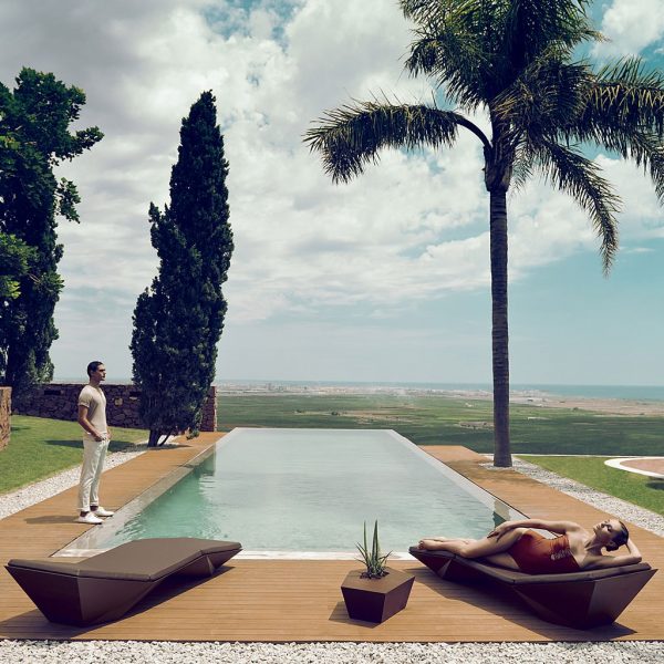 Image of pair of Vondom Faz modern brown sun loungers with swimming pool and palm tree in the background