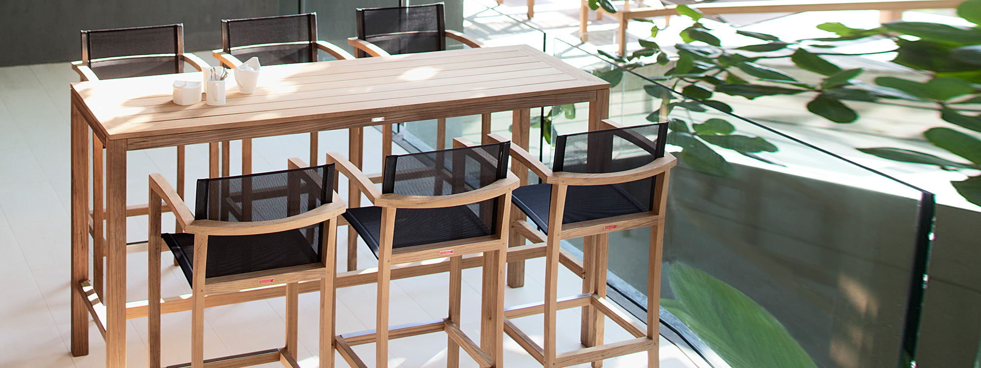 Image of XQI teak bar table and teak bar stools with black Batyline seats and backs by Royal Botania