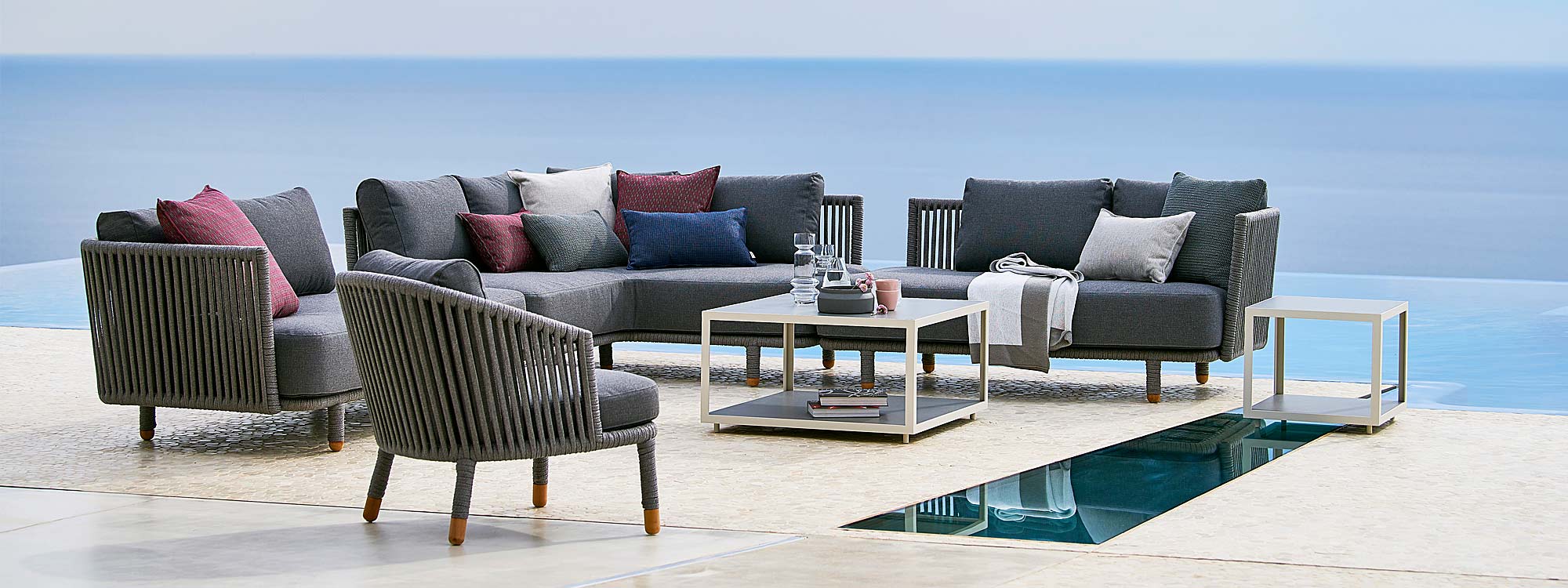 Image of seaside terrace with grey Moments corner sofa and Level outdoor coffee tables by Cane-line