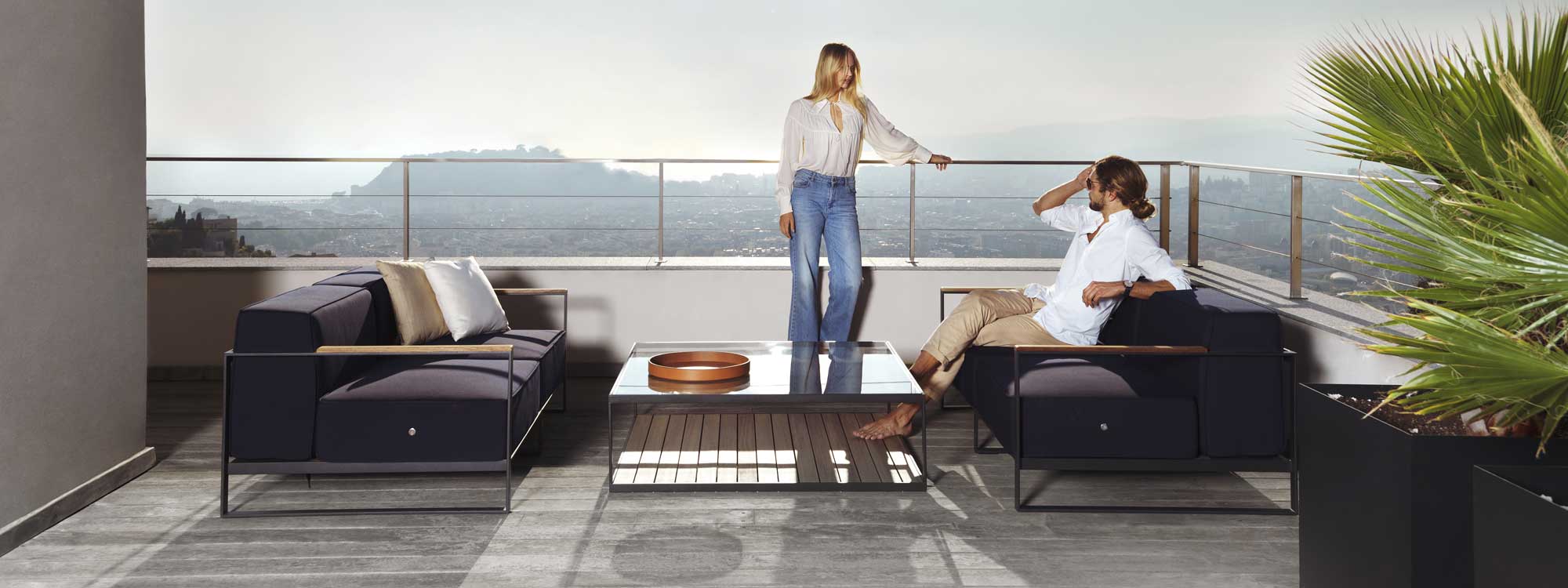 Image of couple relaxing on and around Moore modern garden sofas by Roshults, shown on terrace overlooking hot summer city