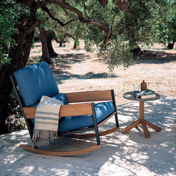 Image of RODA Nap outdoor rocking chair with blue cushions, next to Root side table, with olive trees in the background
