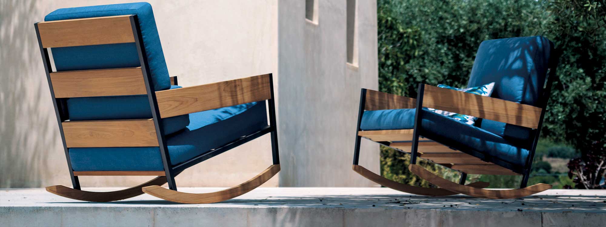Image of pair of RODA Nap modern outdoor rocking chairs and Root side table, in sun and shade on poured concrete terrace