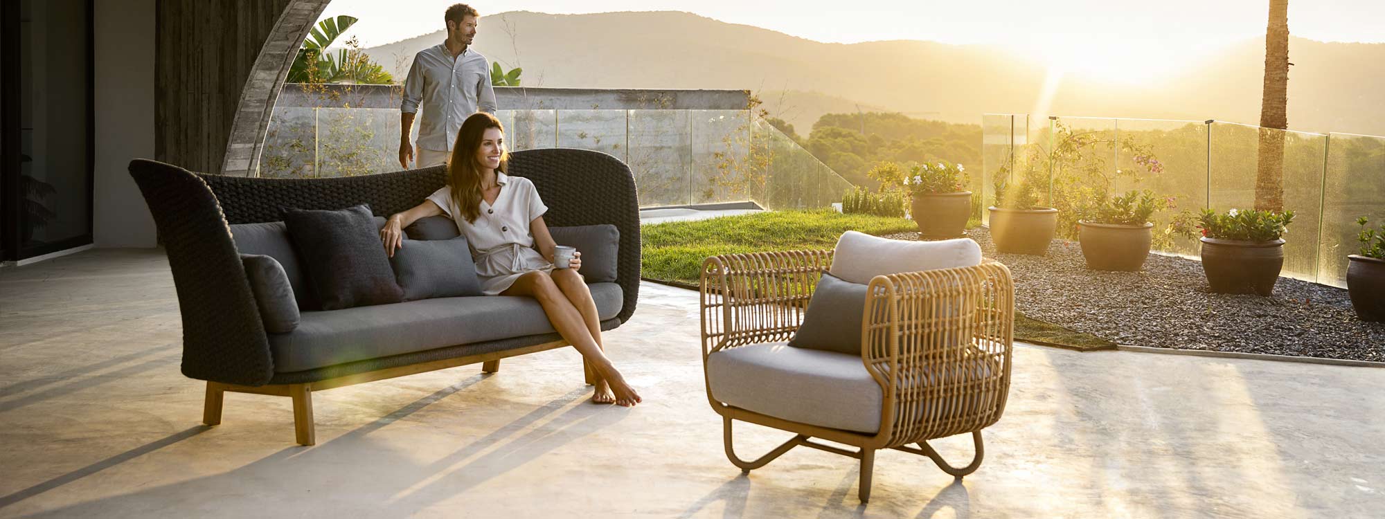 Image of woman sat in Caneline Peacock Wing sofa on terrace in setting sun