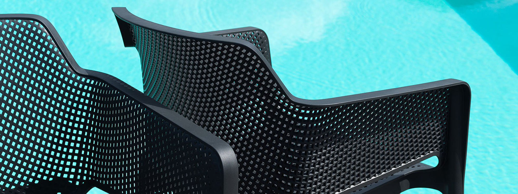 Image of detail of Nardi Net garden chair's black perforated polypropylene back, with azure water of swimming pool in the background