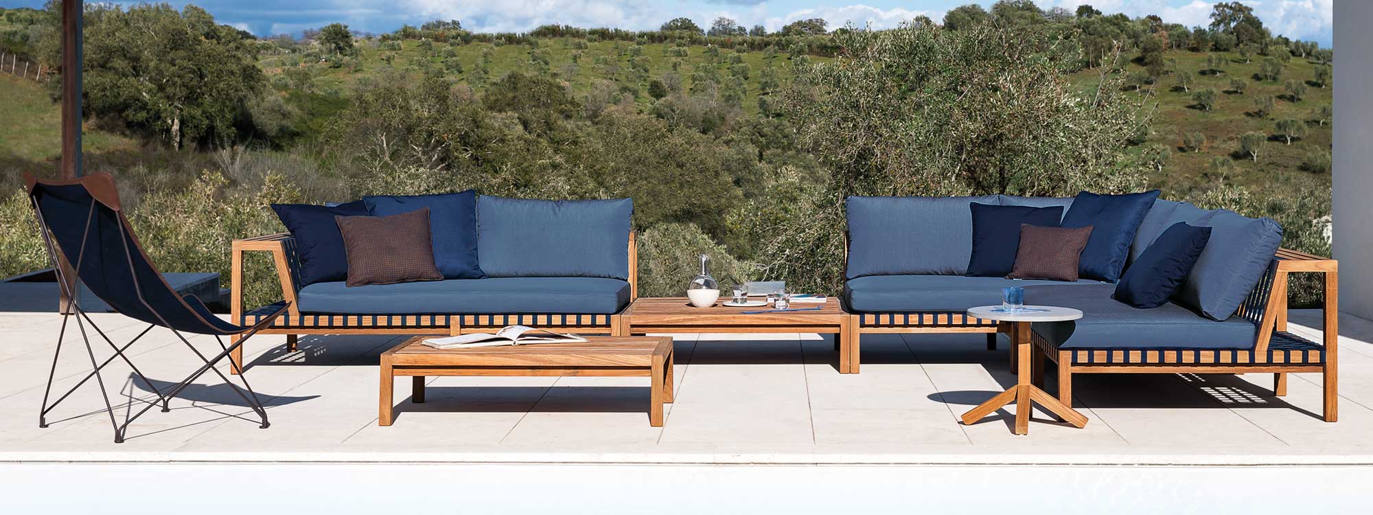 Image of RODA Network teak corner sofa with Blue webbing and Blue cushions with olive orchard in background