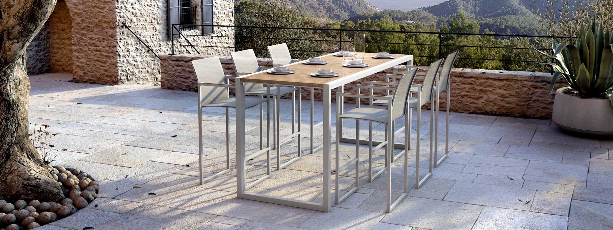 Image of Royal Botania Ninix high table with teak top and bar stools in sand finish on rustic terrace with rolling countryside in background