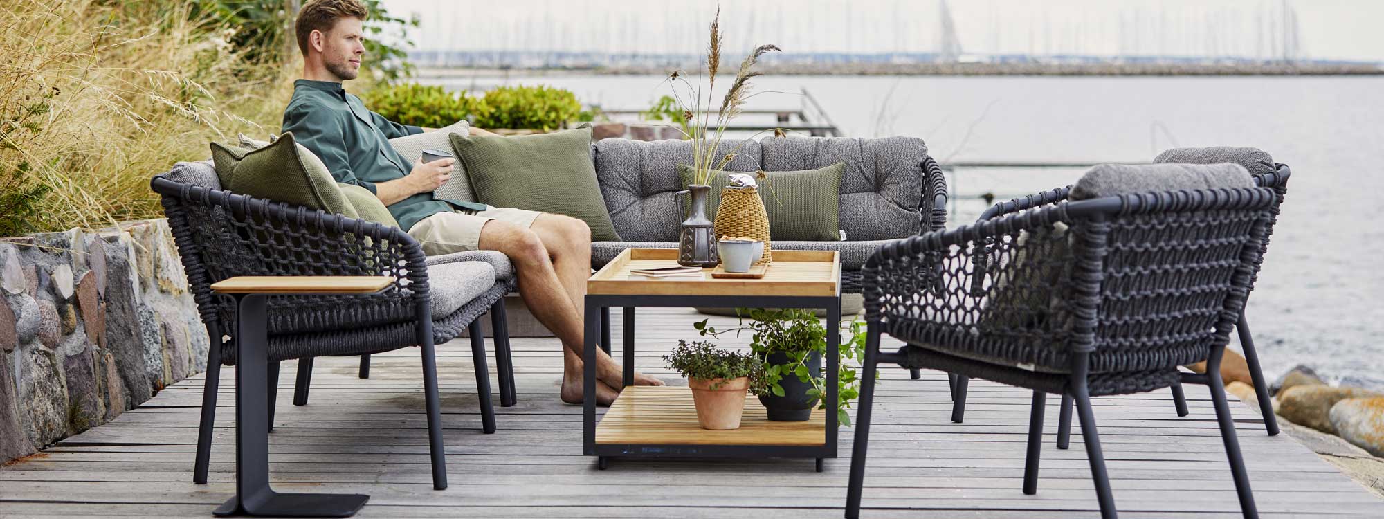 Image of a man sat on Ocean grey outdoor corner sofa around Level low table by Cane-line