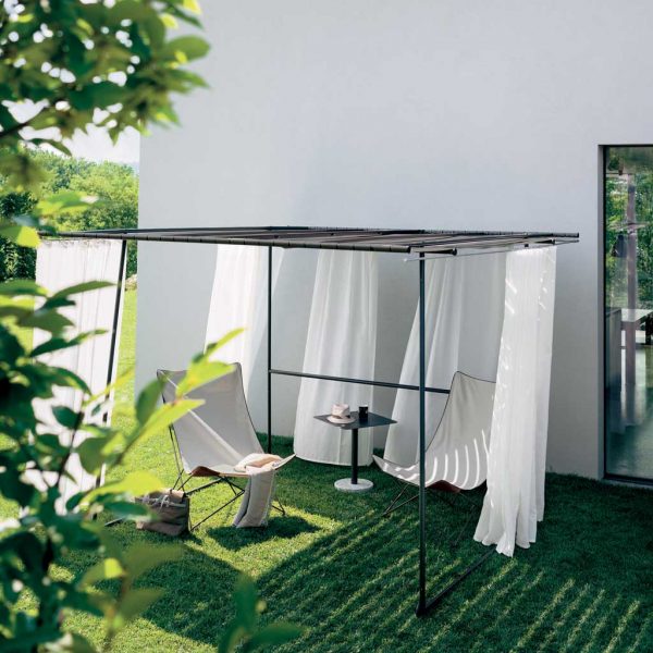 Image of RODA Lawrence outdoor wind chair beneath Ombrina pergola on grassy lawn