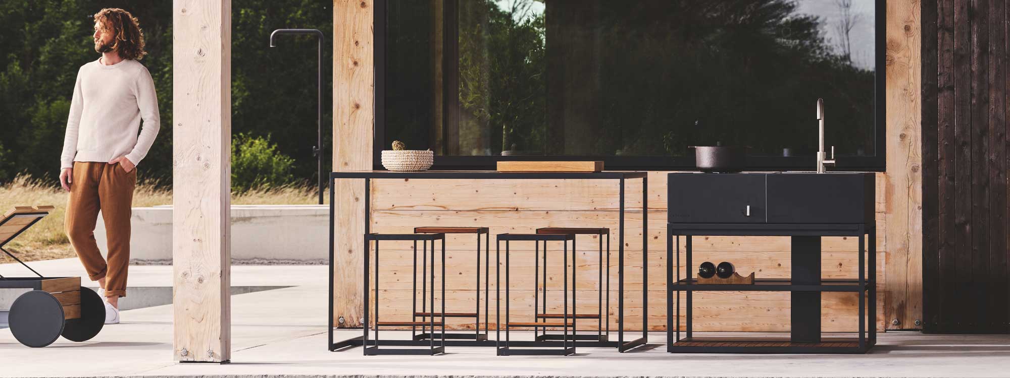 Image of bearded Swedish hipster walking past Roshults Open Bistro high bar table and bar stools shown next to Open Kitchen garden kitchen and bbq