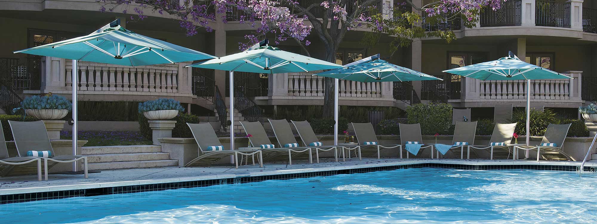 Image of Shademaker Orion side post parasols with turquoise canopies, shown around hotel poolside with sun loungers beneath the parasol canopies