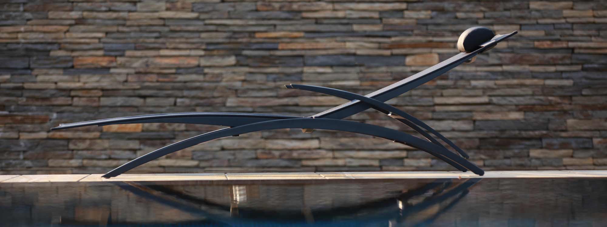 Image of Royal Botania OZN 195T black sun lounger on poolside with dry stone wall in background