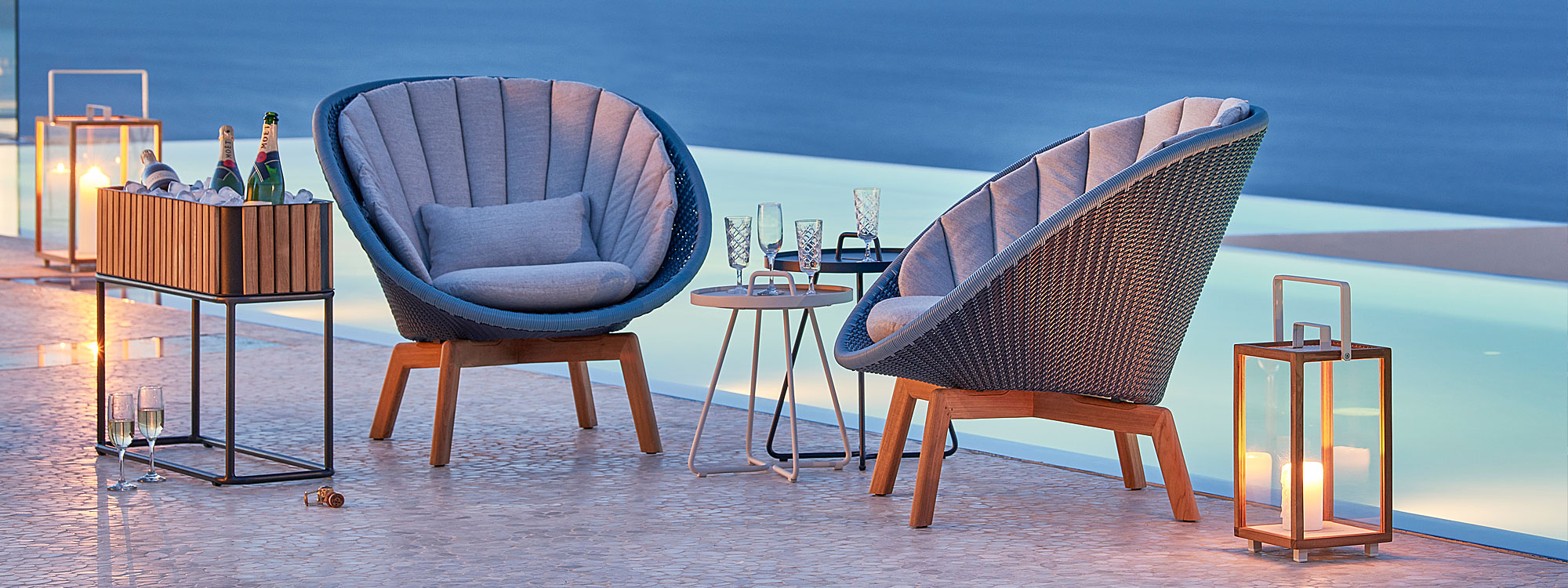 Image of poolside at dusk with Peacock outdoor relax chairs in Cane-line Weave and light-grey cushions
