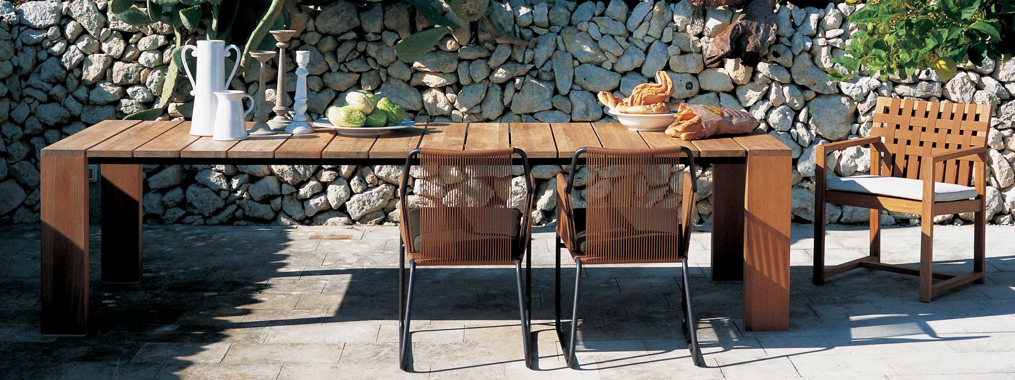 Image of RODA Pier teak table which has bold architectural design, shown together with Harp & Network garden chairs on sunny Italian terrace