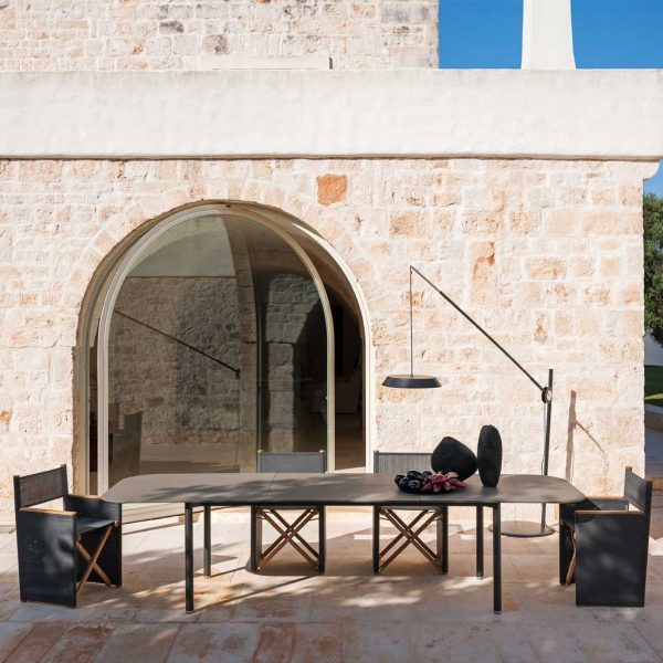 Image of opened RODA Piper extending garden table with Orson folding dining chairs in light and shade of rustic Italian courtyard