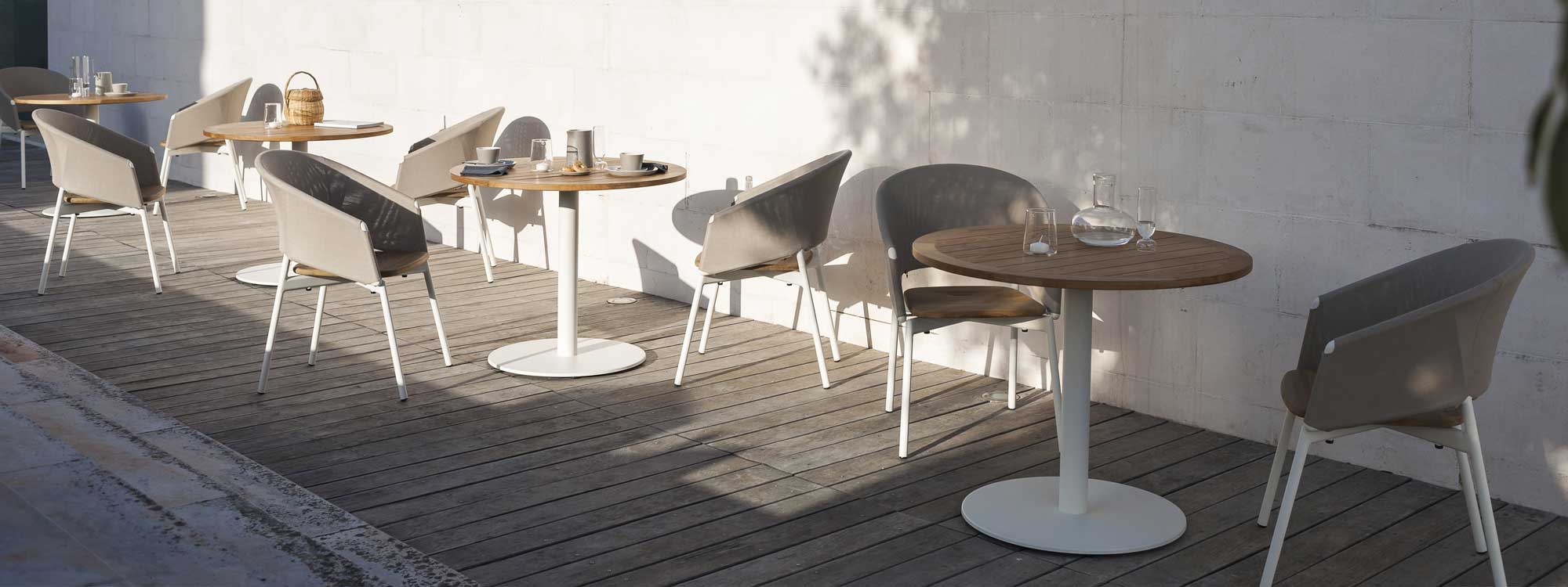 Image of RODA Piper Comfort tub chairs with White frame and Sand Batyline back, together with Stem white bistro tables with circular teak table tops